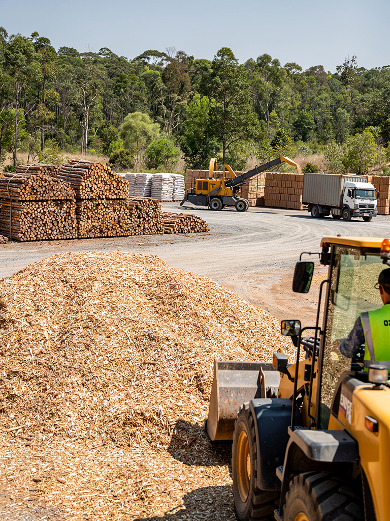 A worker seen from behind operating a wheel loader beside a wood chip pile in the biomass yard.